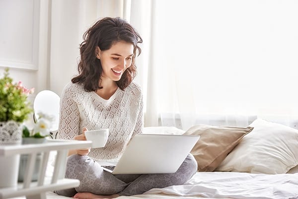 A woman smiling as she reads something on her notebook computer