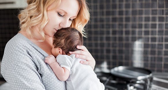 A mother holding her baby inside a kitchen